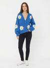 Model wearing a bright blue, button-front knit cardigan decorated with large white and yellow daisy appliques.