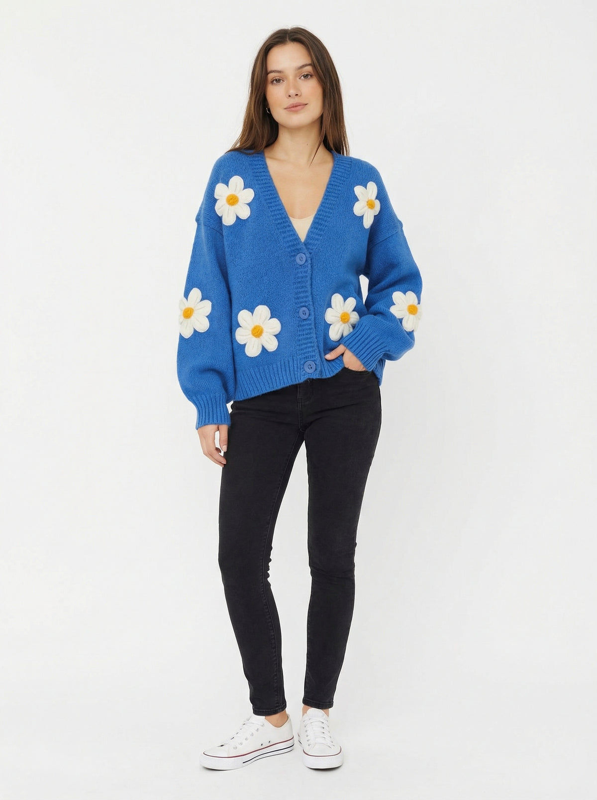 Model wearing a bright blue, button-front knit cardigan decorated with large white and yellow daisy appliques.