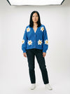 Model wearing a bright blue button-up knit cardigan featuring large white daisy appliques with yellow centers.