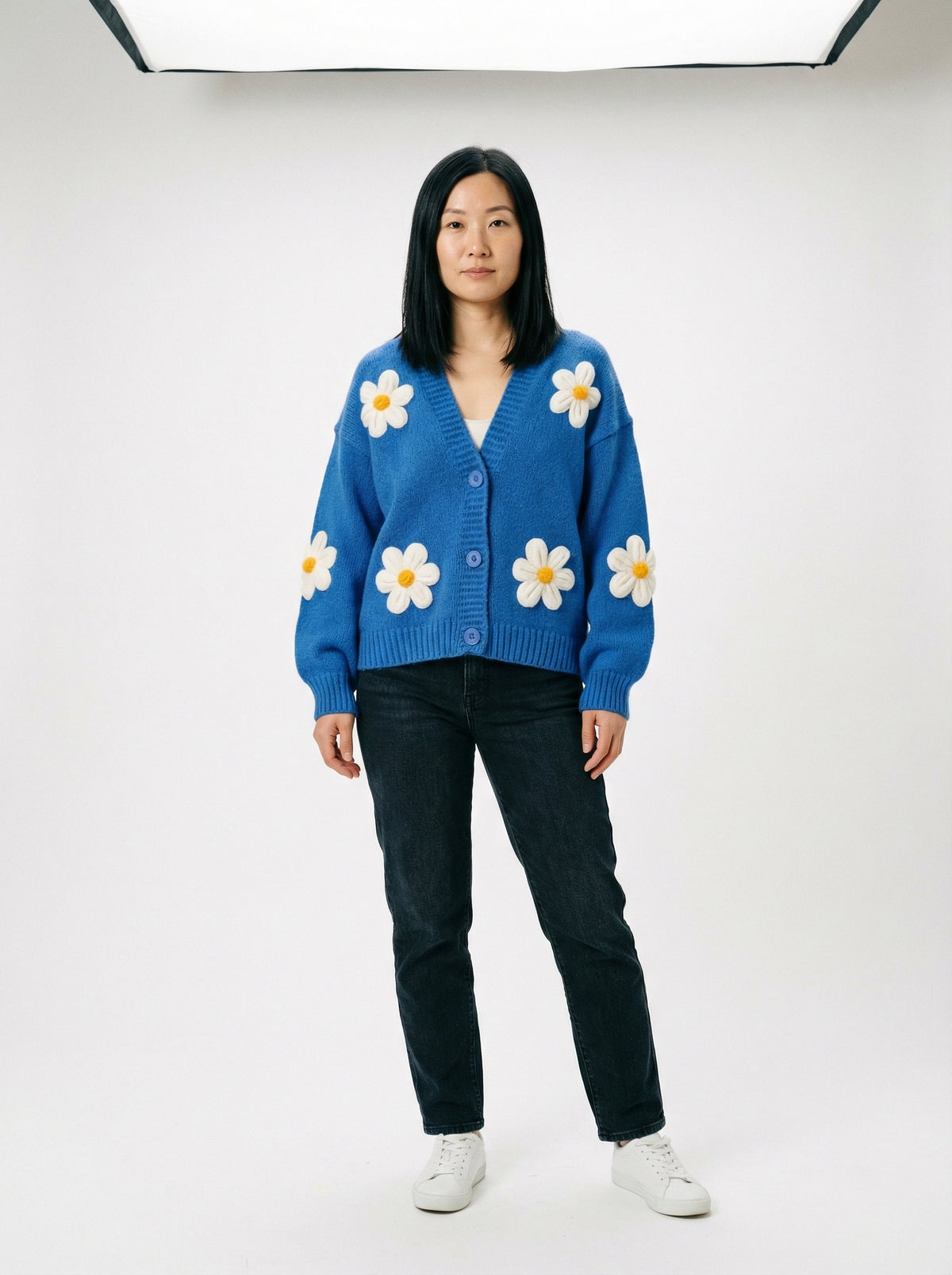 Model wearing a bright blue button-up knit cardigan featuring large white daisy appliques with yellow centers.