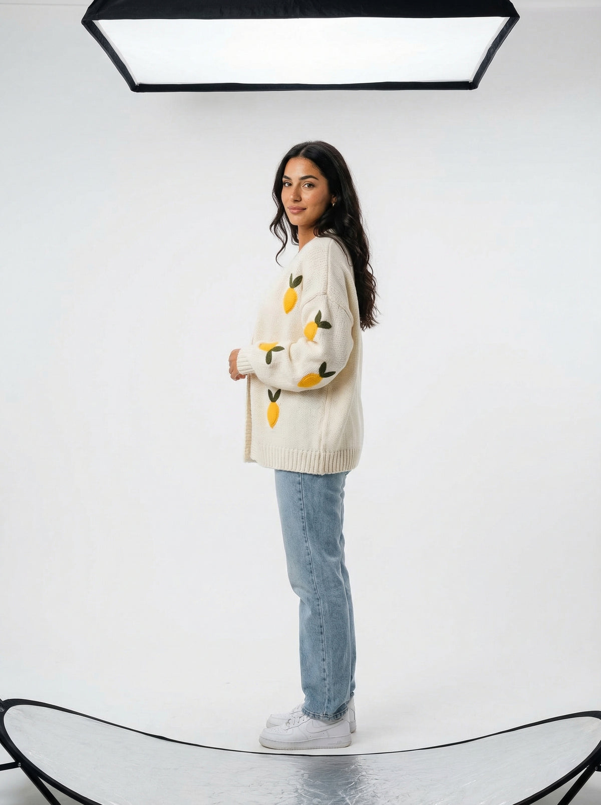 Woman wearing an off-white knit cardigan with yellow lemon appliques and green leaves, paired with light blue jeans.